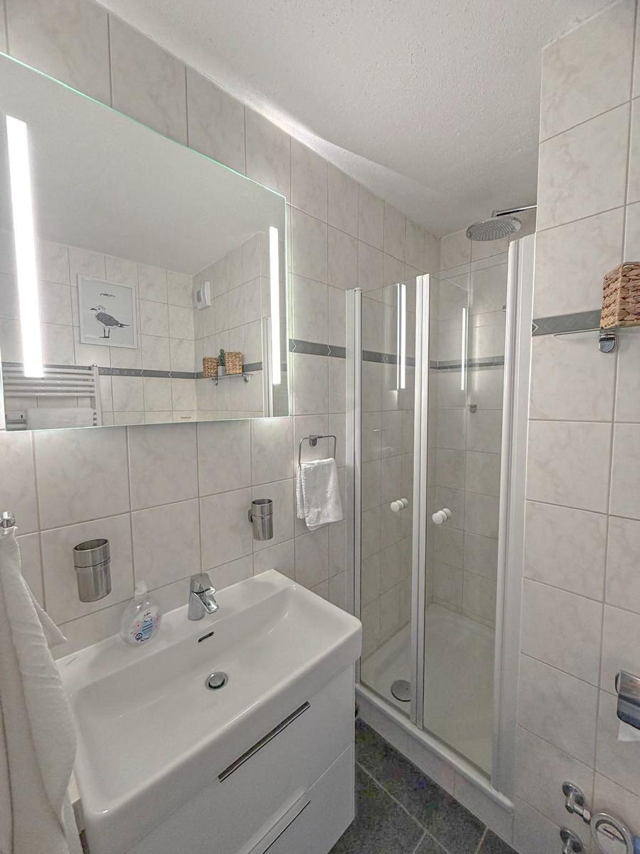 Badezimmer mit Dusche, Waschbecken und beleuchtetem Spiegel