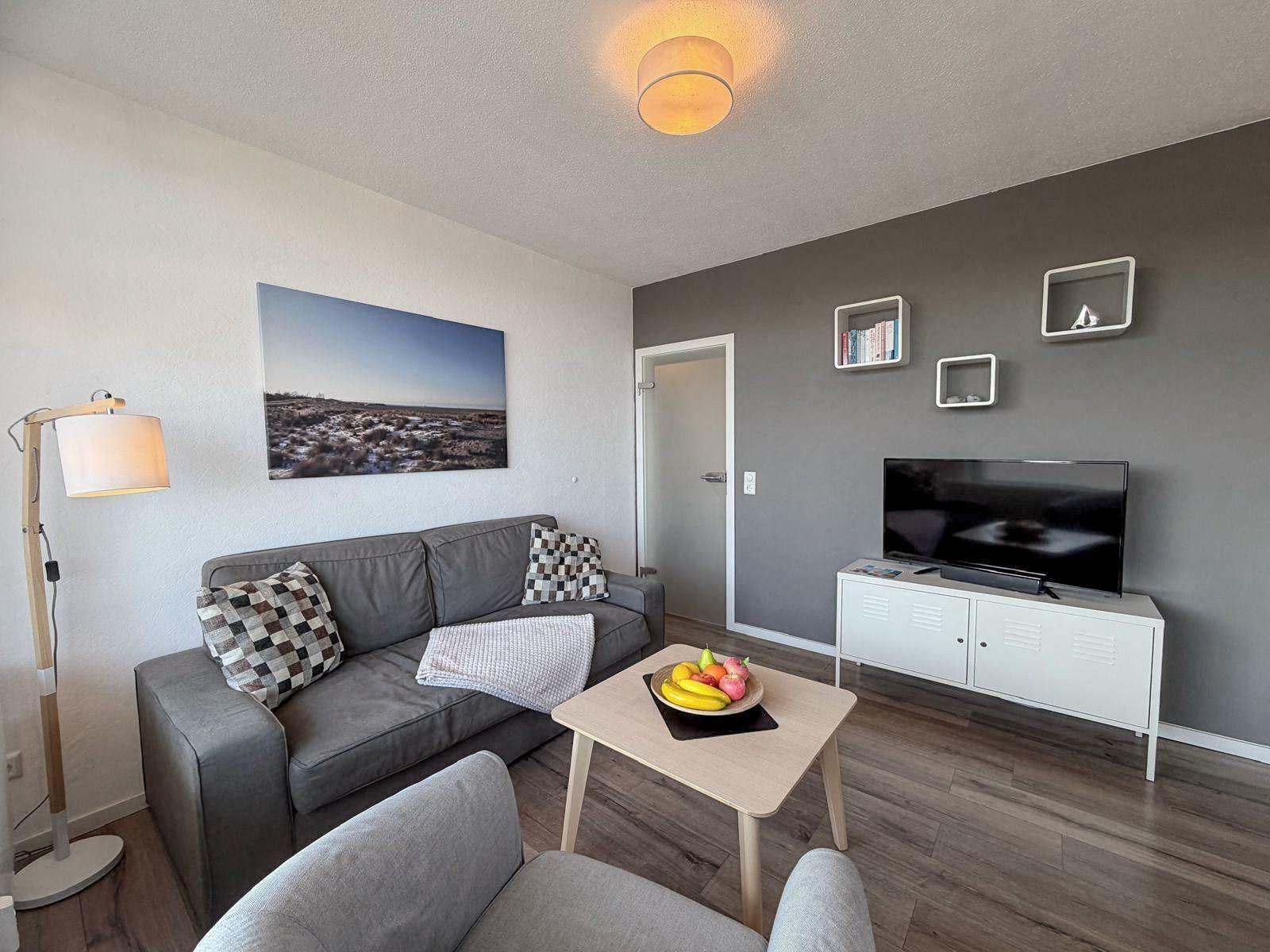 Wohnzimmer mit Sofa, Fernseher und Tisch mit Obst.