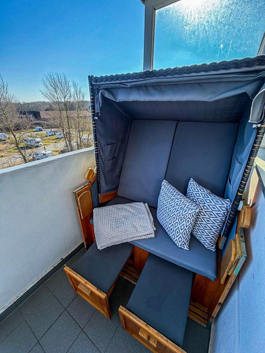 Terrassenliege mit blauer Polsterung und Kissen auf Balkon mit Blick auf Campingplatz.