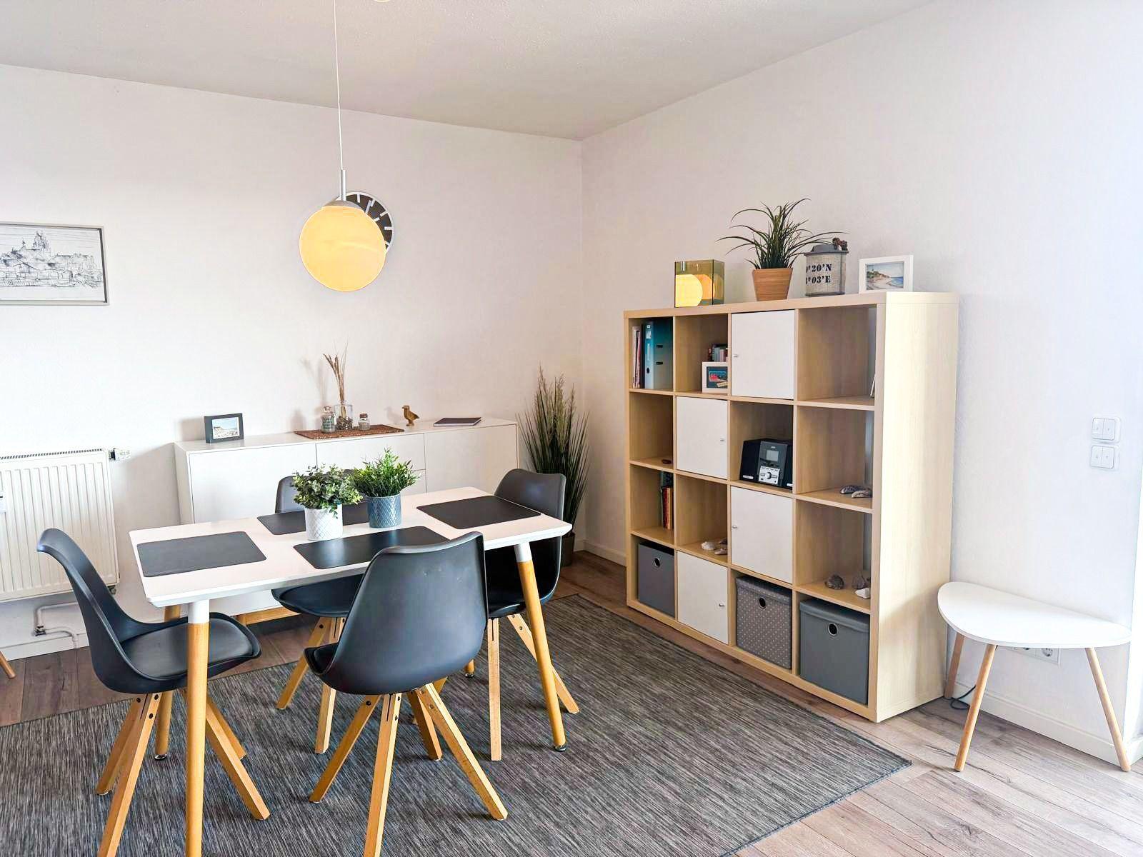 Esszimmer mit Tisch, Stühlen und Regal. Helle Wände und Holzboden.