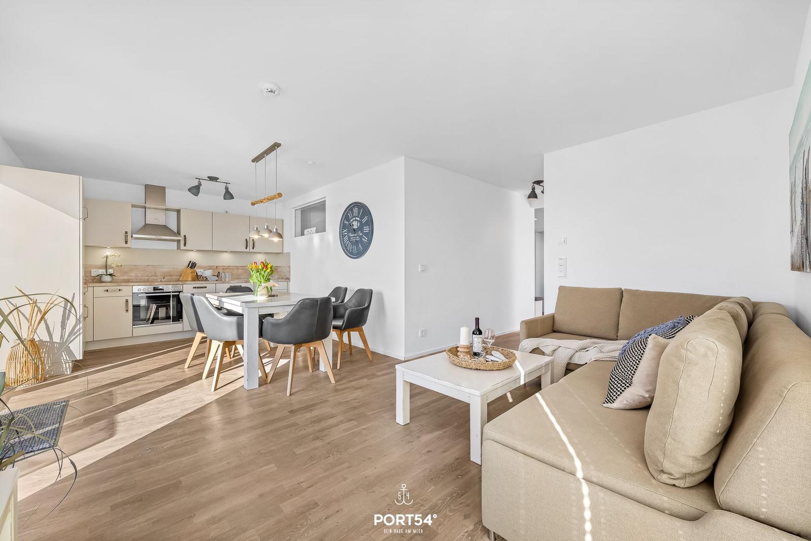 Wohn- und Essbereich mit Küchenzeile und Sofa. Holzboden und helle Wände.