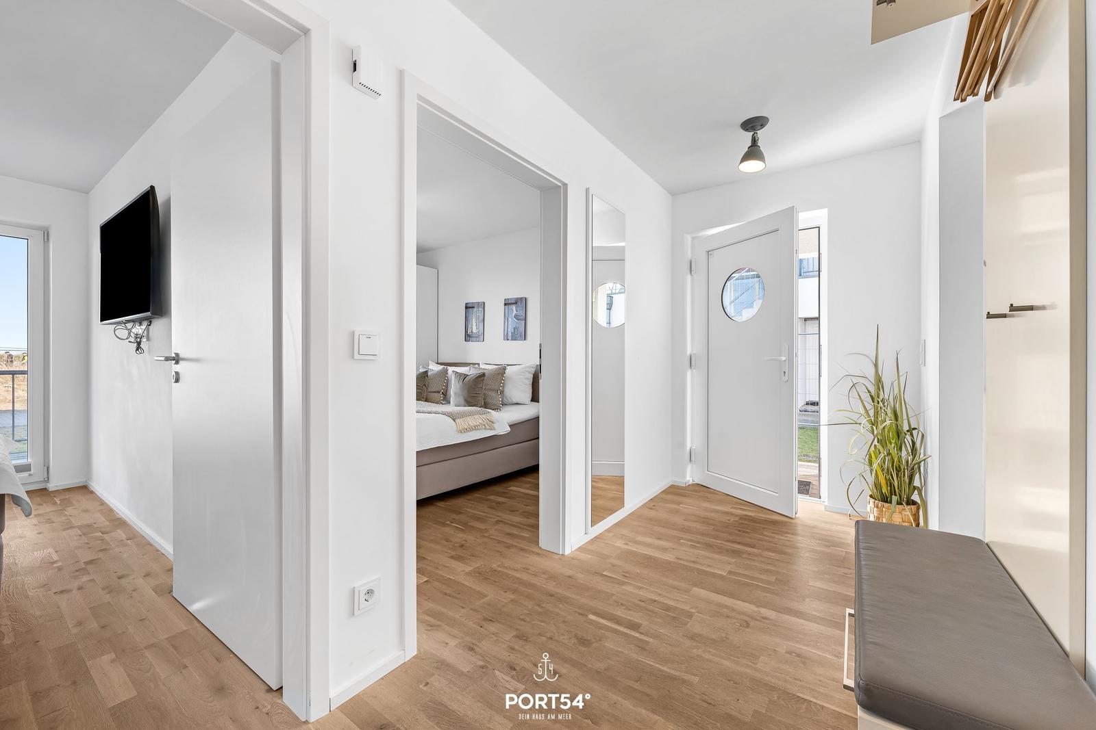 Flur mit Holzboden, Schlafzimmer und Tür mit runden Fenster.