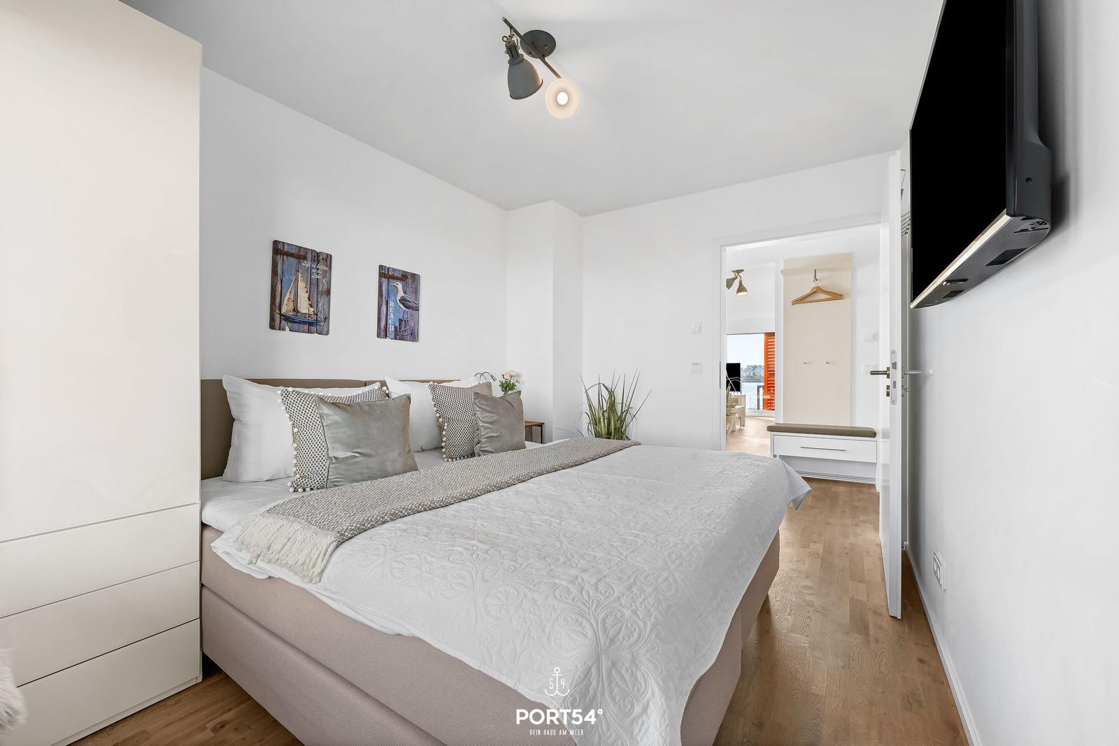Schlafzimmer mit Bett, Kleiderschrank und Fernseher an der Wand.