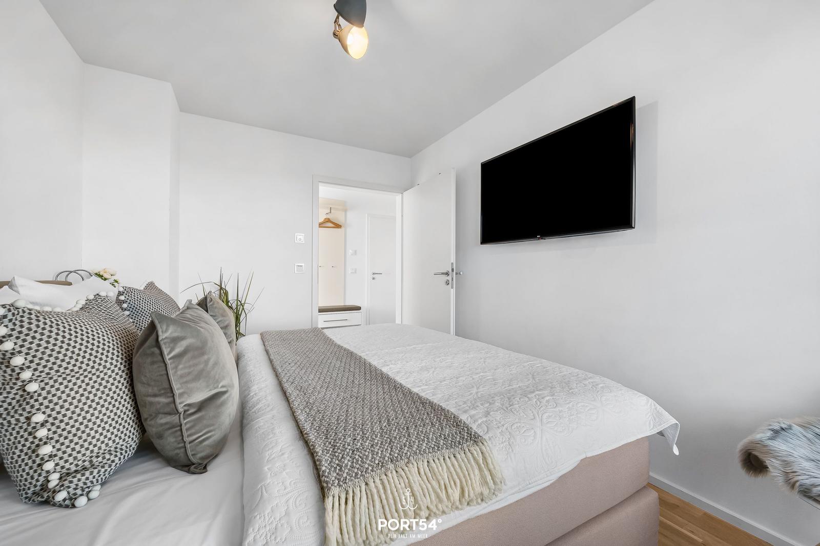 Schlafzimmer mit Bett, Wandfernseher und Pflanze.