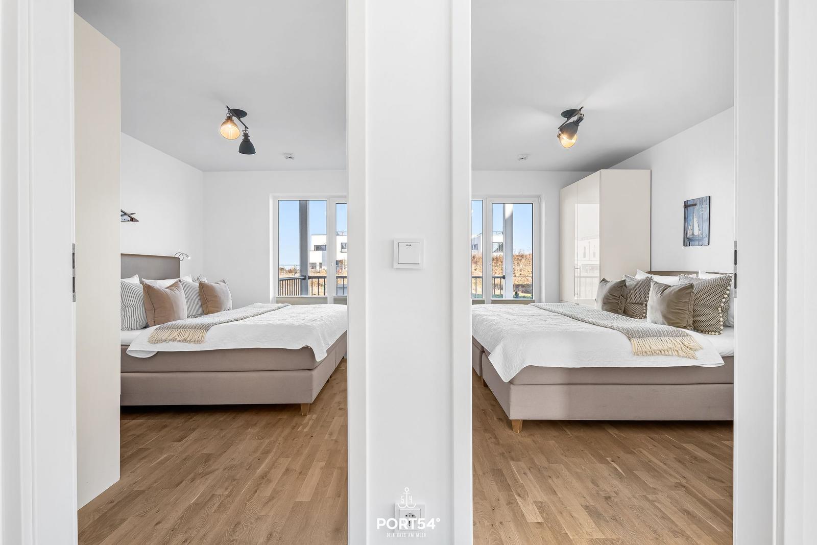 Zwei Schlafzimmer mit Betten, Holzboden und Fenstern zum Balkon.