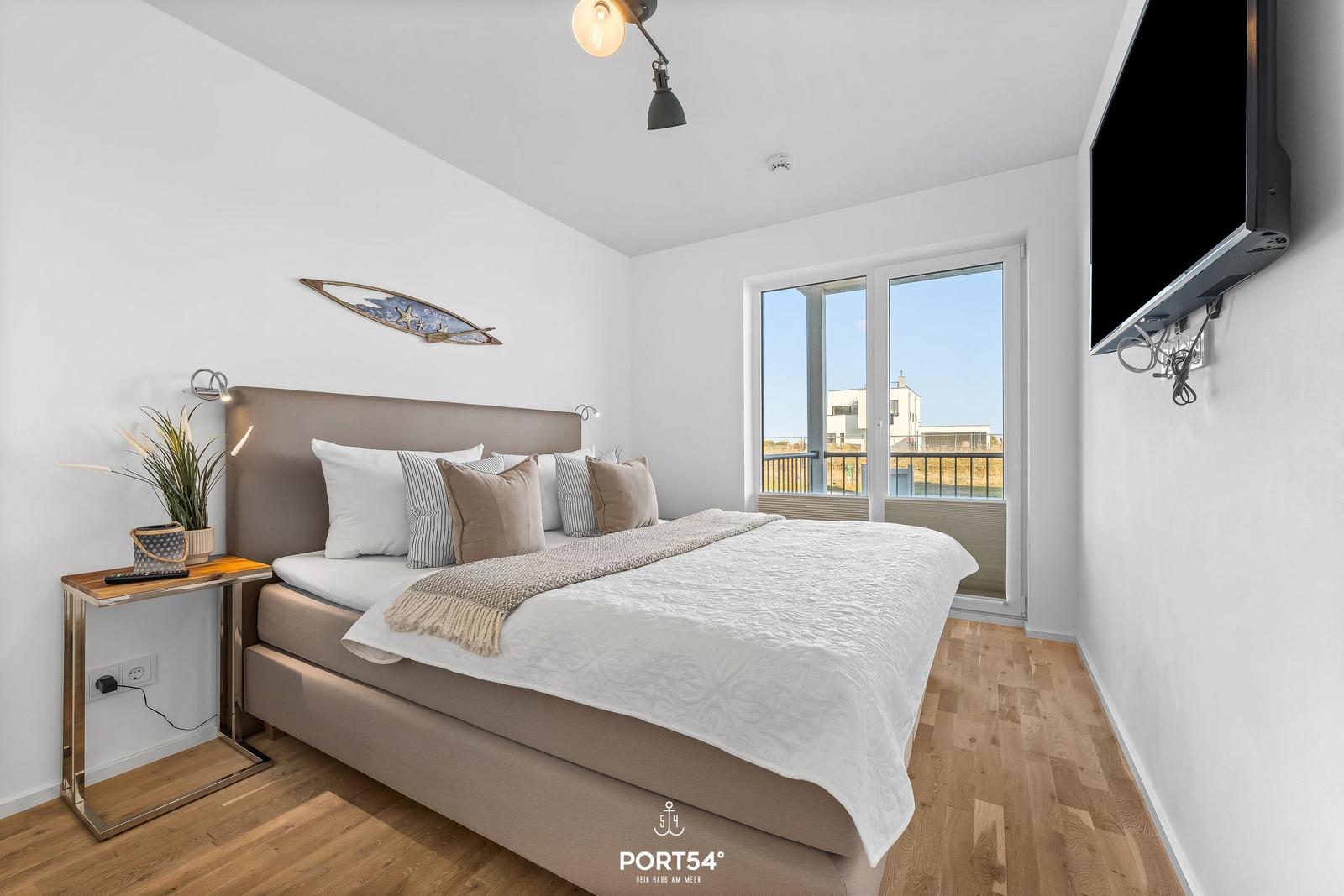 Schlafzimmer mit Doppelbett, TV und Balkonansicht.