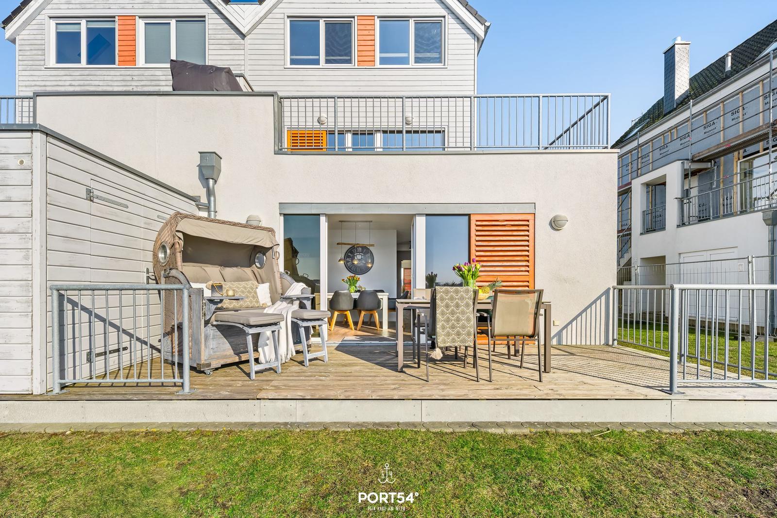 Terrasse mit Sitzgruppe und Esstisch. Durchgang in Wohnbereich mit Tisch und Stühlen.