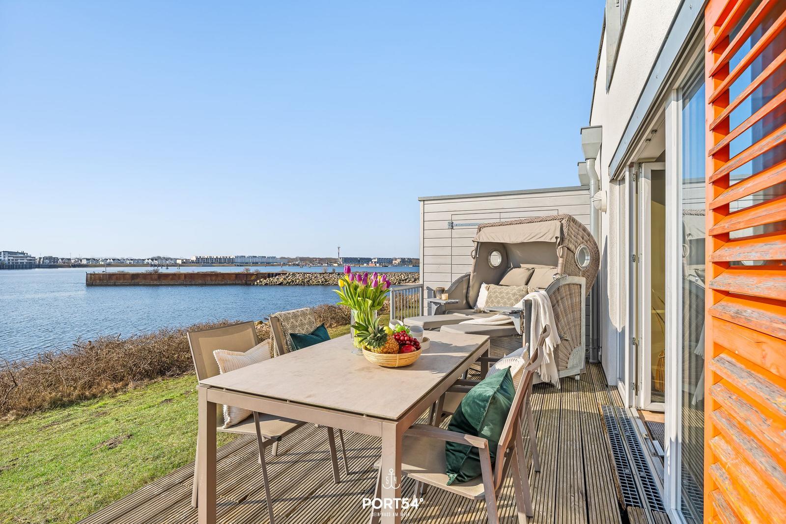 Terrasse mit Tisch, Stühlen und Liege direkt am Wasser.