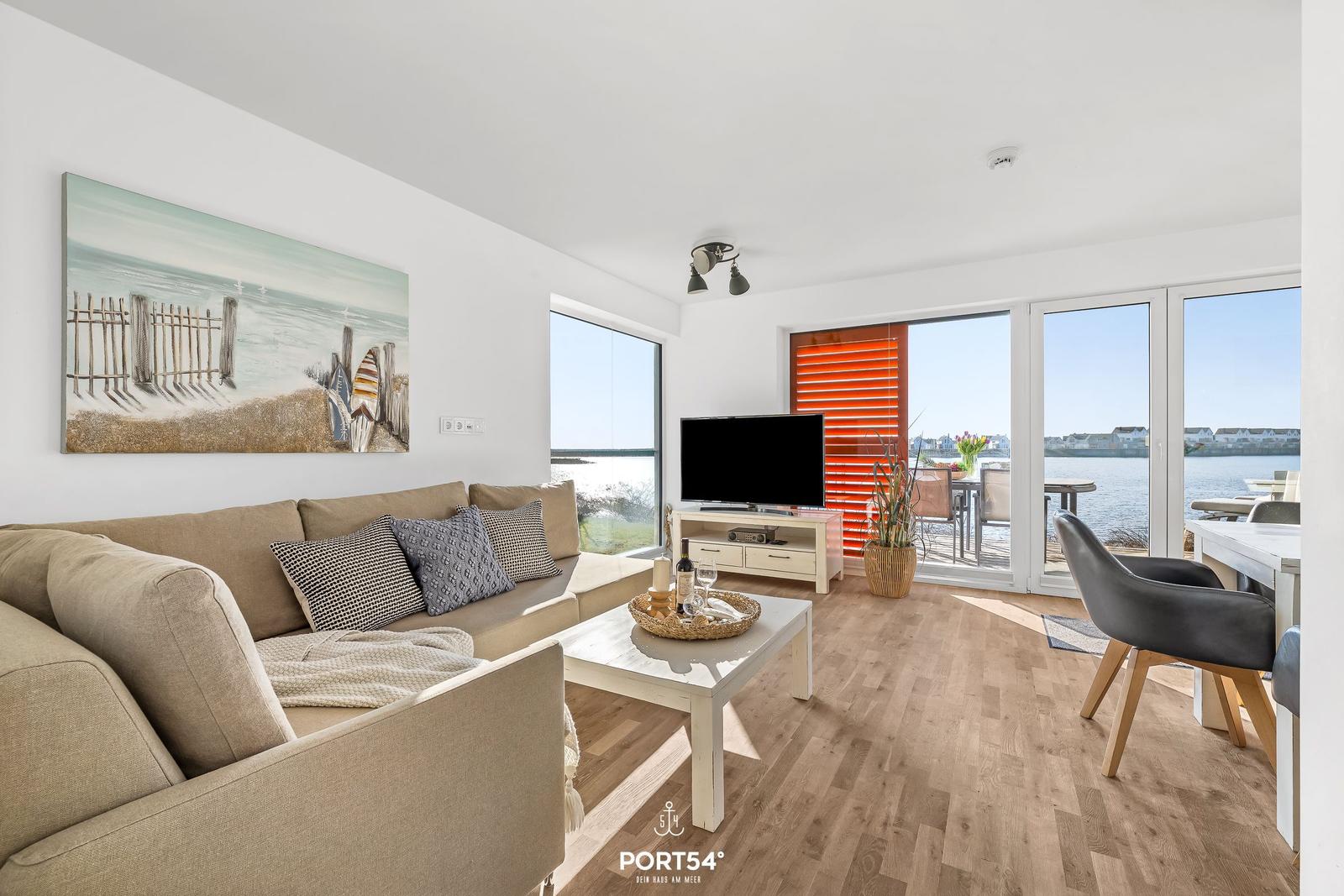 Wohnbereich mit Sofa, TV und Blick aufs Wasser.