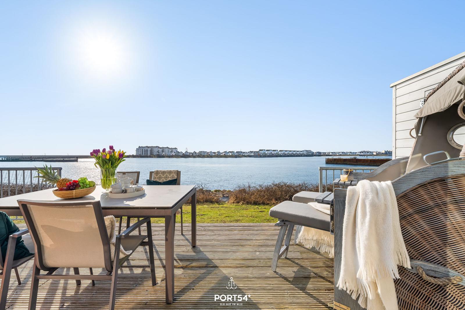 Terrasse mit Tisch, Stühlen und Blick auf Wasser und Ufer