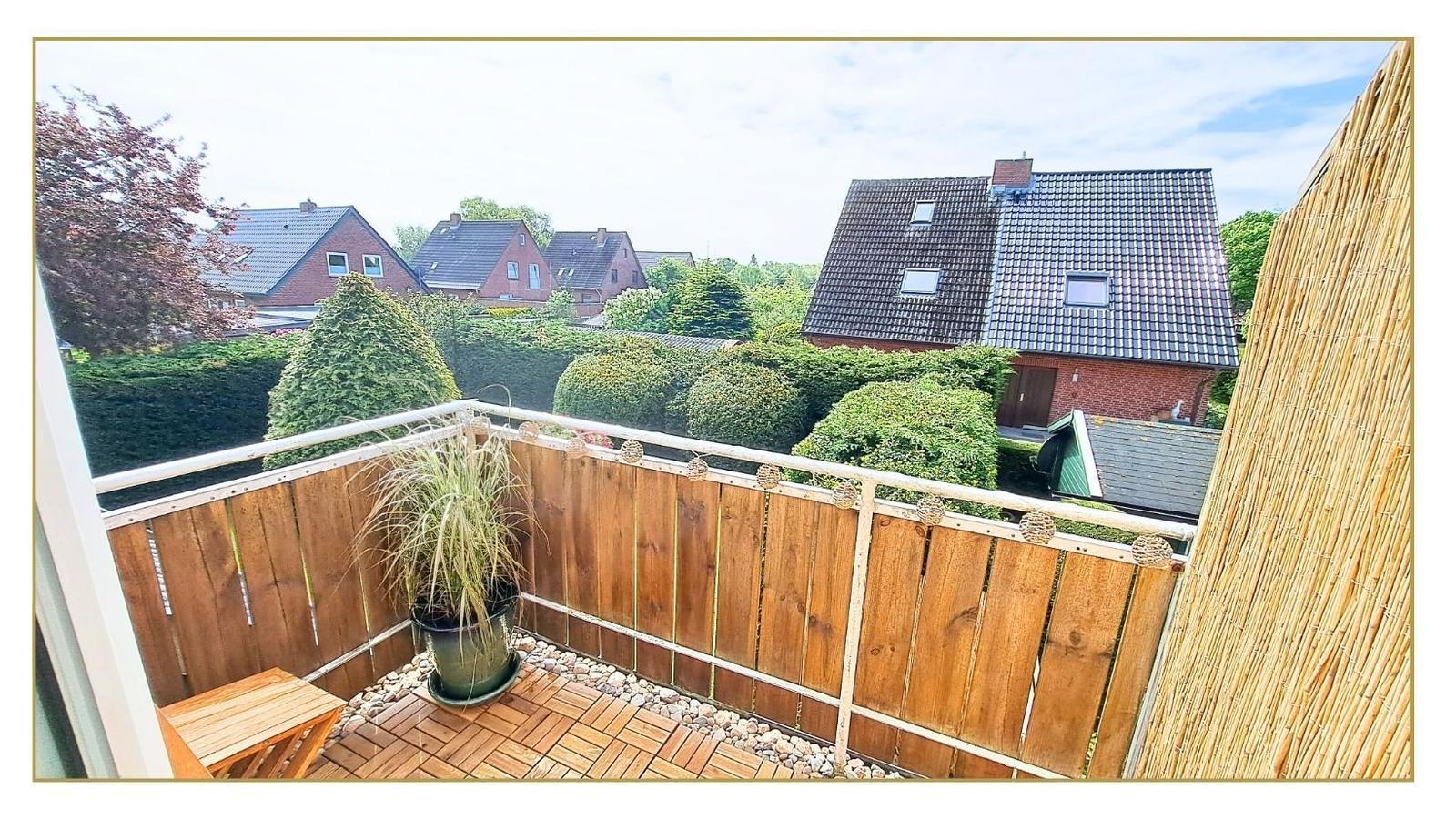 Terrasse mit Holzbelag, Pflanze und Sicht auf umliegende Häuser und Bäume.