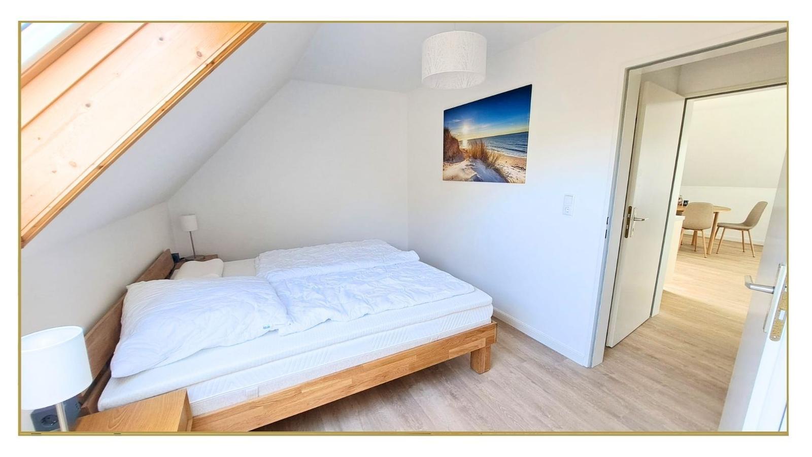 Schlafzimmer mit Dachschrägen, Bett, Wandbild und Tür zum Flur.