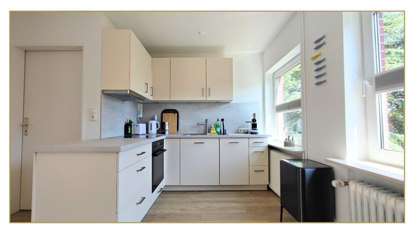 Moderne Küche mit weißen Schränken, Arbeitsplatte und Fensterblick.