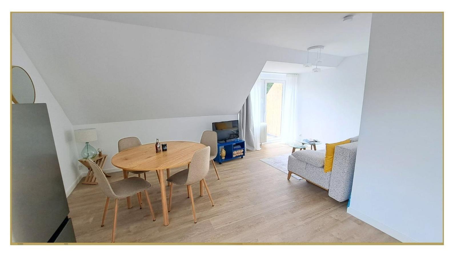 Wohn- und Essbereich mit Holztisch, Sofa und TV. Dachschräge und Holzboden.
