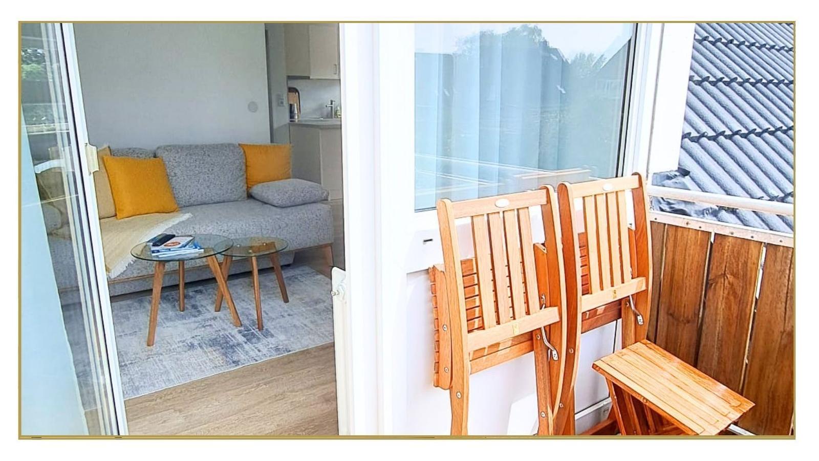 Balkon mit zwei Holzstühlen und Tisch. Im Hintergrund Wohnbereich mit Sofa und Tisch.