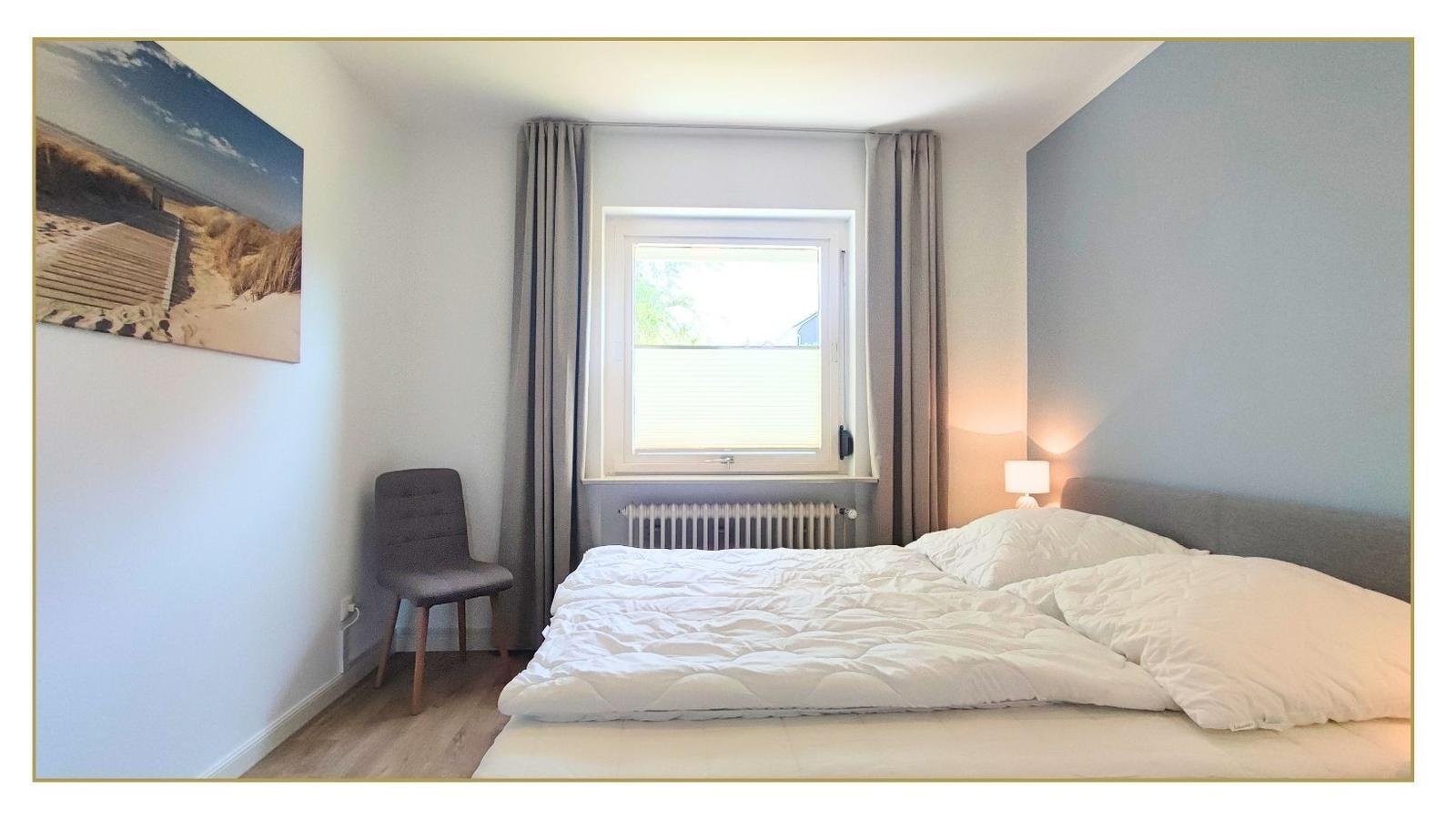 Schlafzimmer mit Bett, Fenster, Vorhängen und Wandbild.