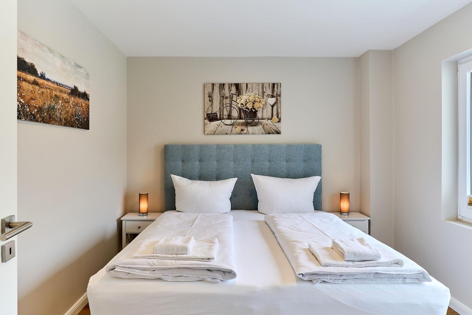 Schlafzimmer mit Doppelbett, zwei Nachttischen und Wandbildern.