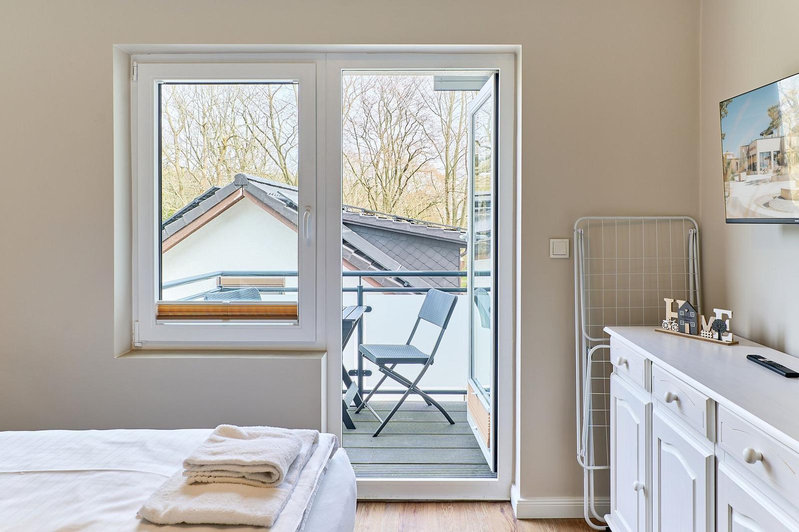 Schlafzimmer mit Balkon, Bett, Schrank und Fernseher.