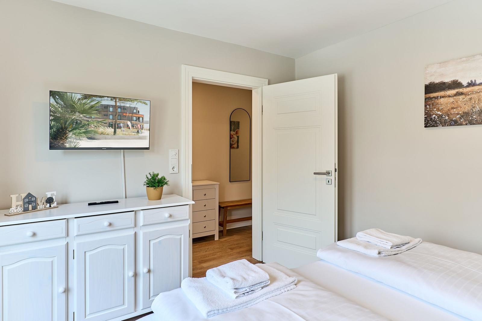 Schlafzimmer mit Bett, TV und Kleiderschrank. Tür führt in angrenzenden Raum.
