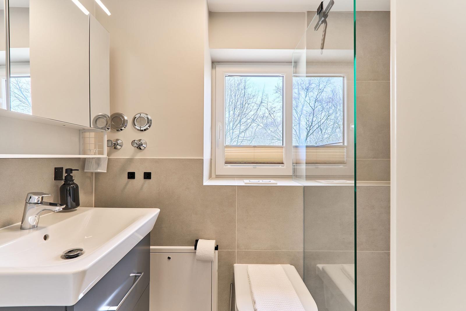 Badezimmer mit Waschbecken, Dusche und Fenster. Modern eingerichtet.