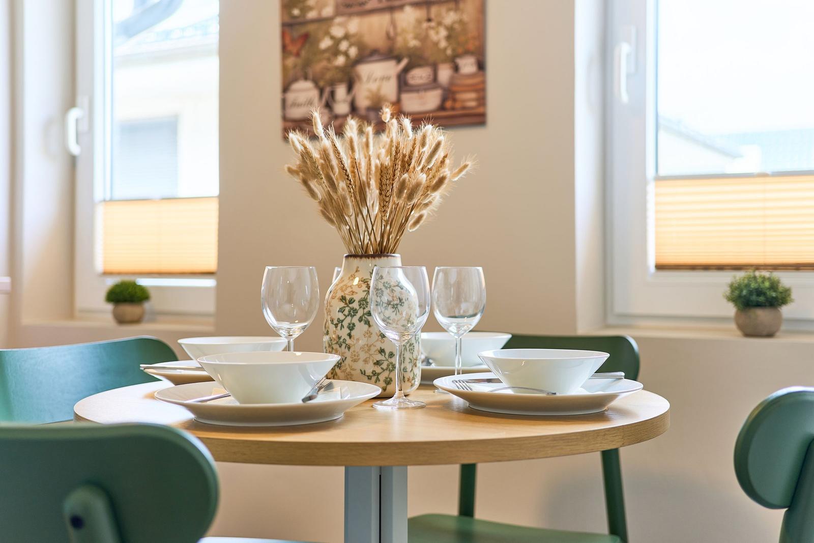 Rundes Esszimmer mit Tisch, Stühlen und dekorativer Vase mit Getreideähren.