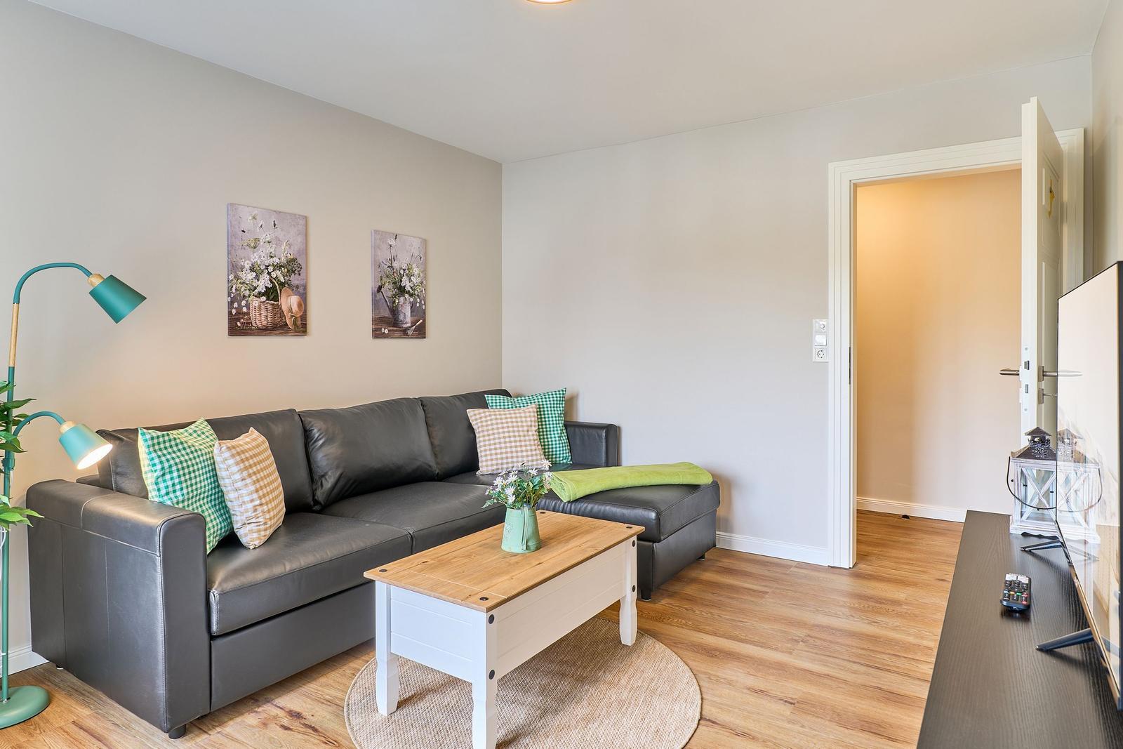 Wohnzimmer mit grauem Sofa, Holztisch und Wandbildern.