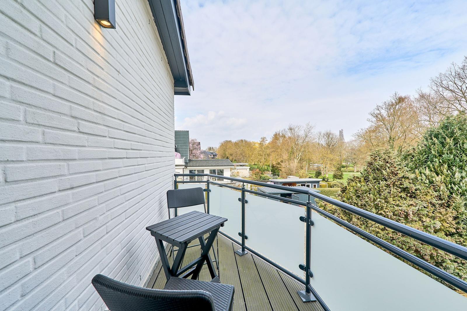Balcony with table and chairs overlooking greenery and trees.