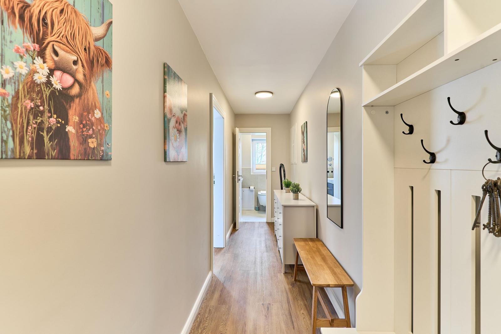 Flur mit Wandbildern, Spiegel, Badezimmer und Holzbank.