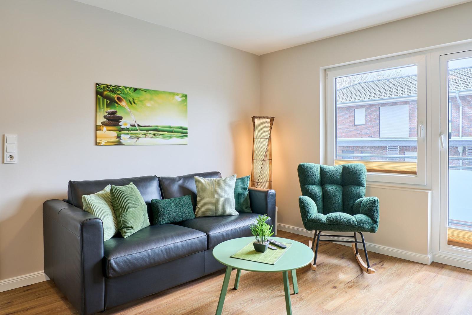 Wohnzimmer mit Sofa, Sessel und Tisch. Wandbild und Fenster sichtbar.