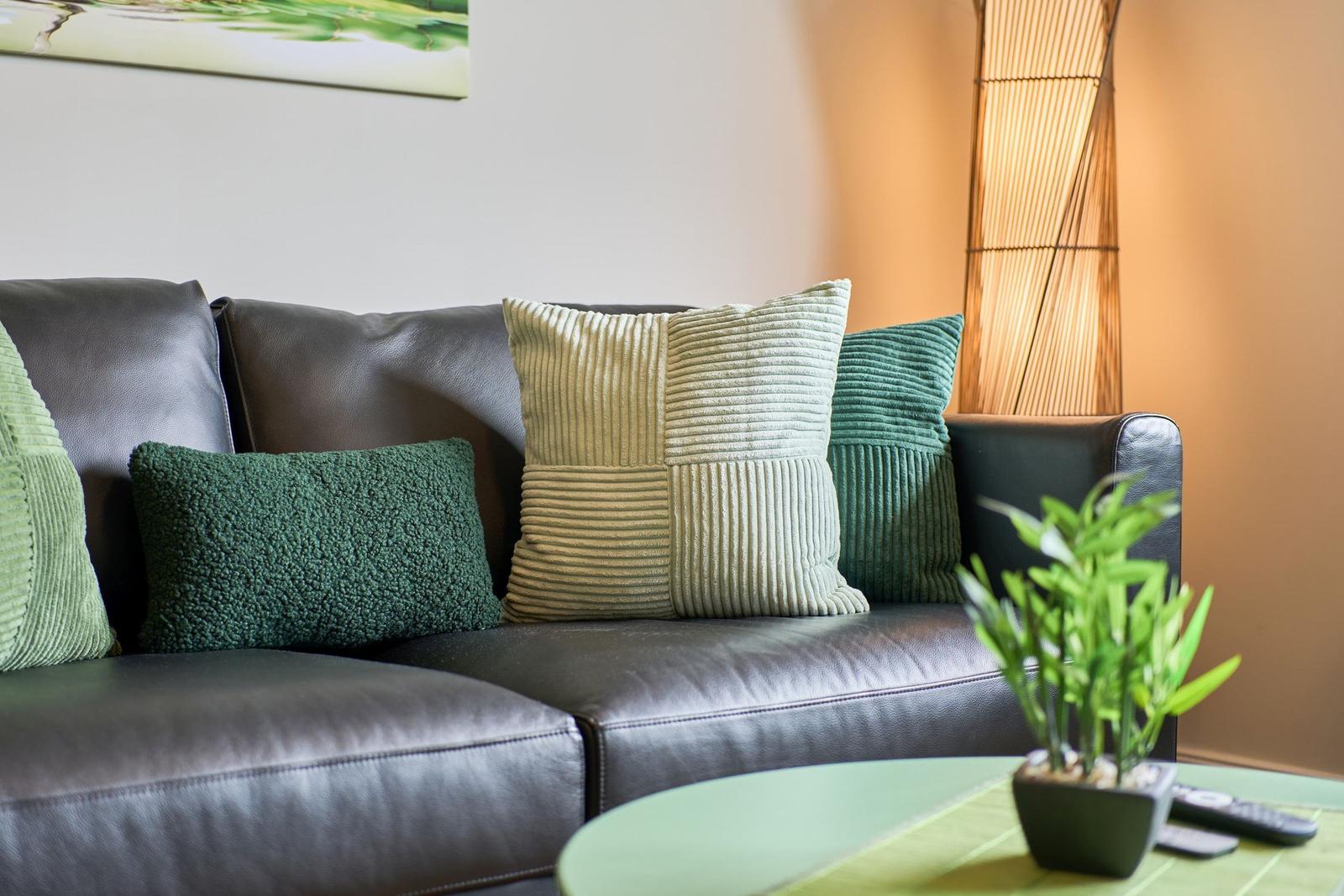 Schwarzes Ledersofa mit grünen Kissen und Pflanze auf Tisch.