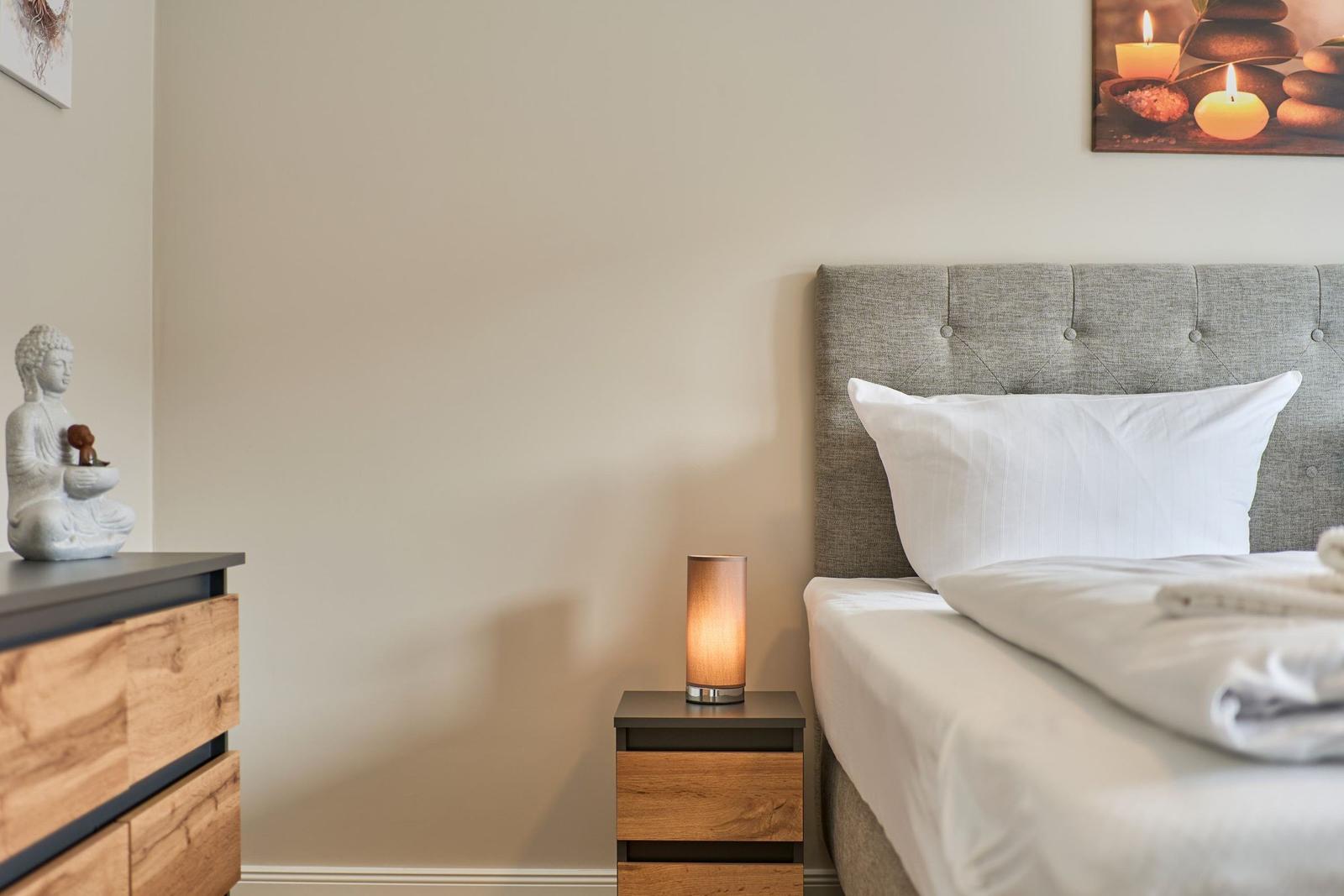 Schlafzimmer mit Bett, Nachttisch und Schrank. Wandbild und Buddha-Statue sind sichtbar.