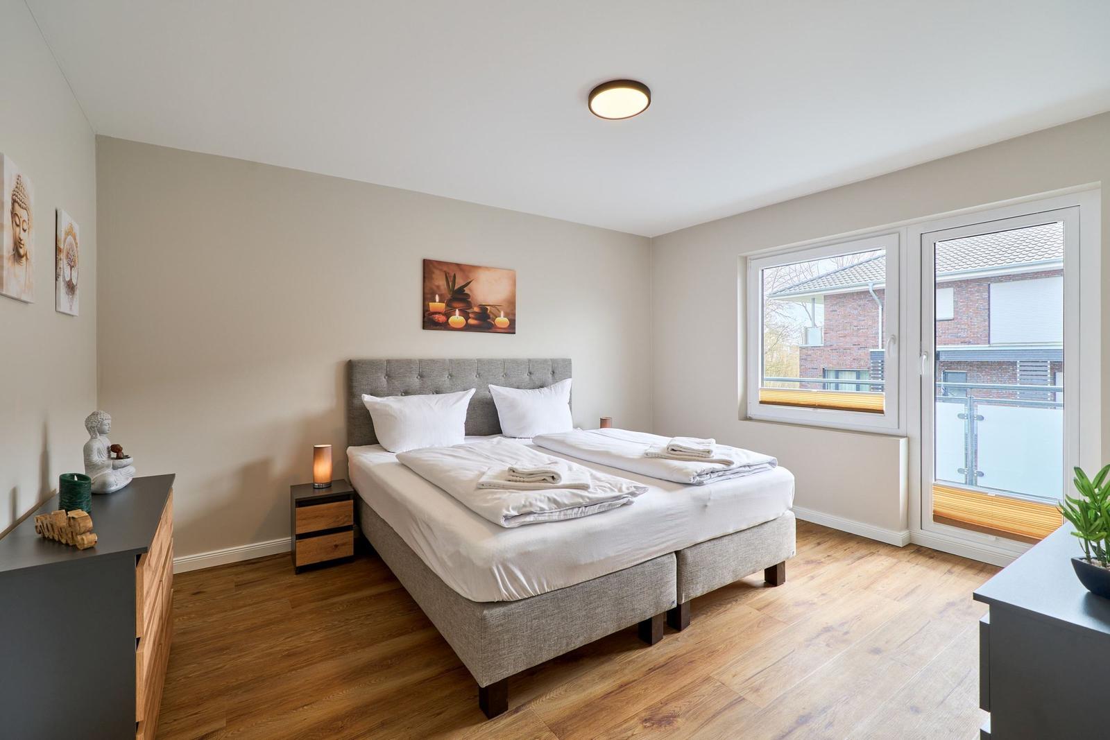 Schlafzimmer mit Doppelbett, Holzboden und Balkontür. Wandbild und Buddha-Statue sind sichtbar.