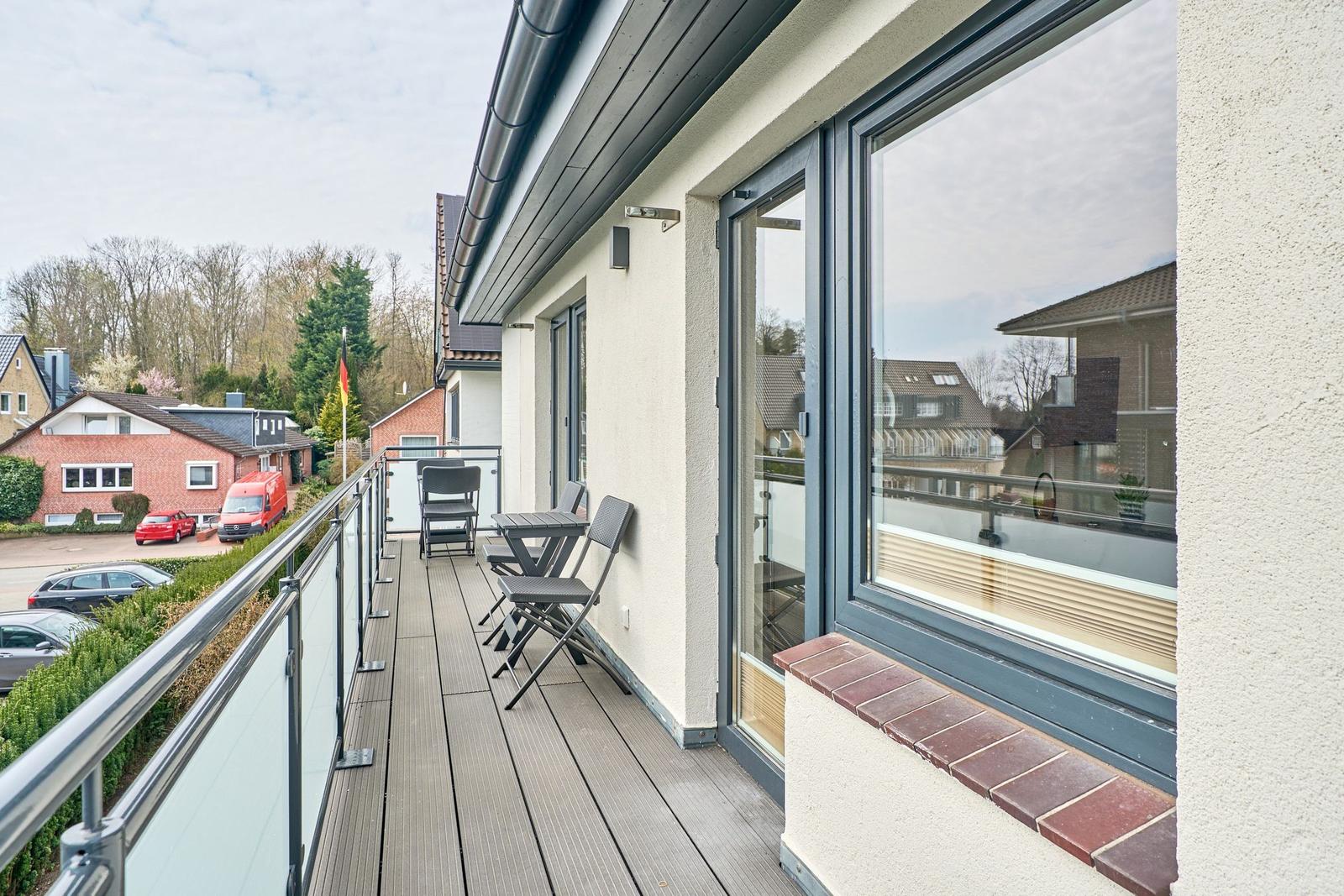 Terrasse mit Tisch und Stühlen, Glasgeländer und Blick auf Wohnhäuser.