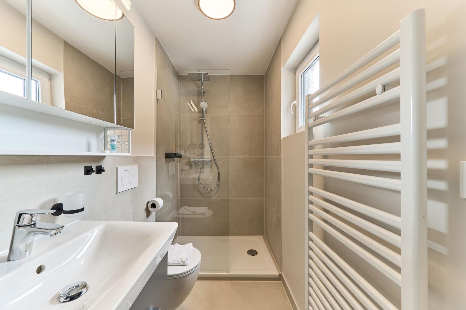 Badezimmer mit Dusche, Waschbecken und Heizkörper