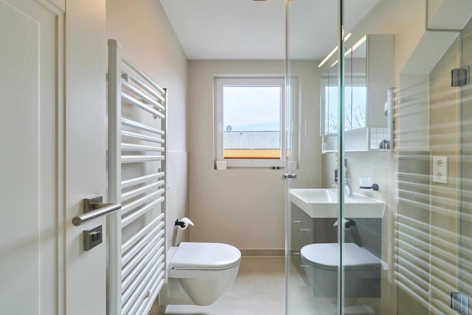 Badezimmer mit Dusche, Waschbecken und Toilette. Fenster mit Blick auf Dach.