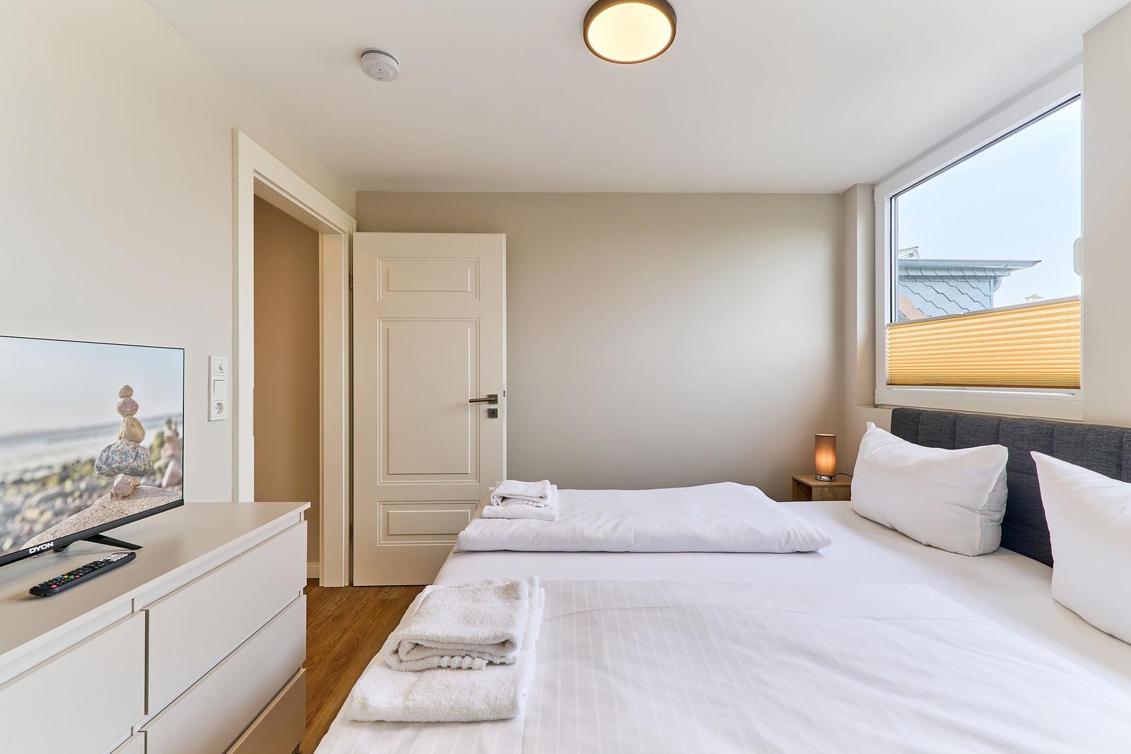 Schlafzimmer mit Bett, Fernseher und Fenster. Handtücher auf dem Bett.