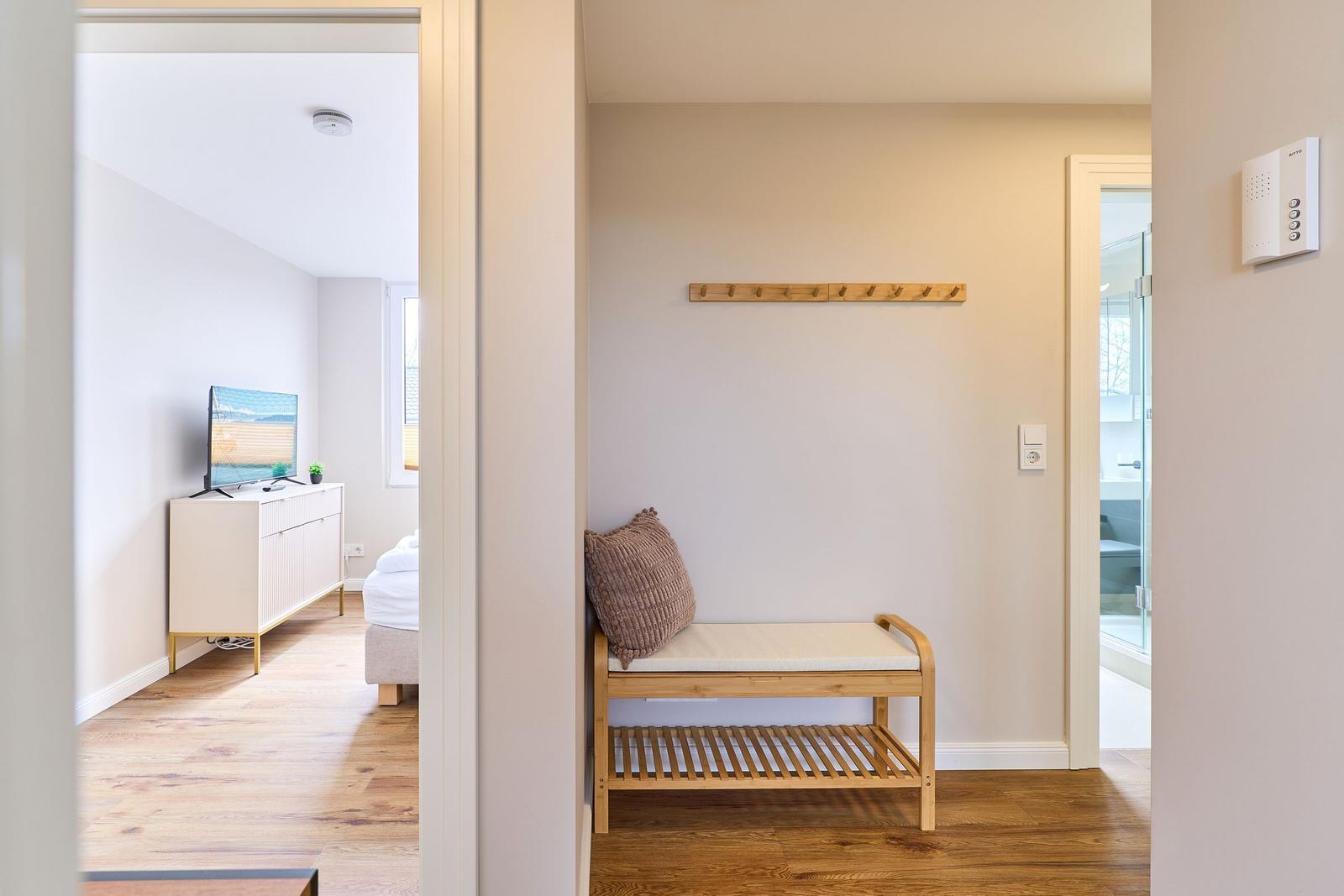 Eingangsbereich mit Holzbank, Kleiderhaken und Blick in Schlaf- und Badezimmer.