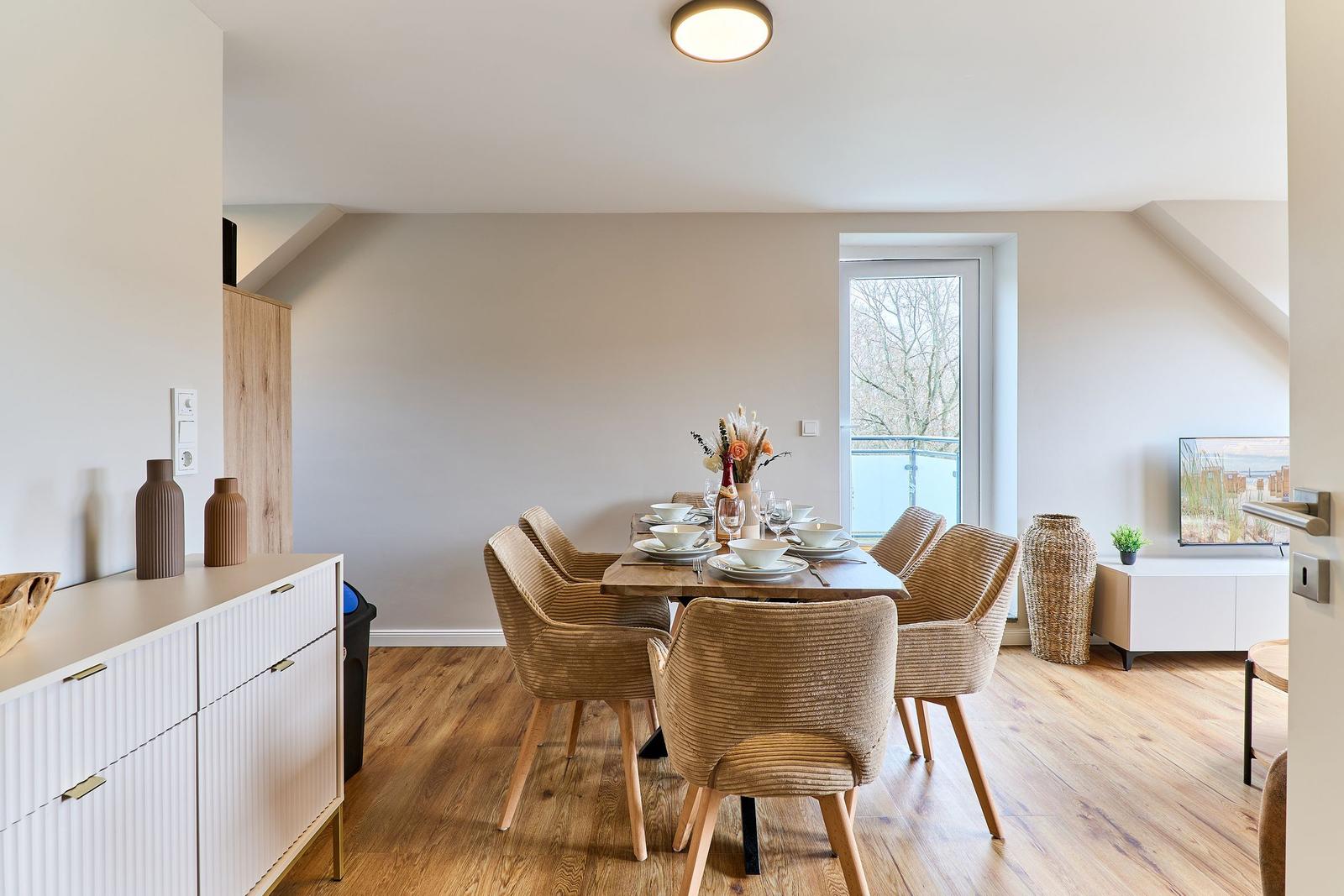 Esszimmer mit Holztisch, sechs Stühlen und Fenster zum Balkon.