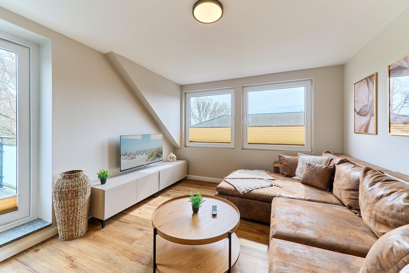 Wohnzimmer mit braunem Sofa, runden Tisch und TV auf weißem Sideboard.