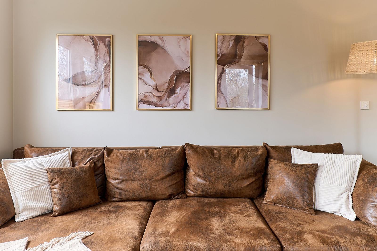 Ein braunes Sofa mit Kissen und drei Wandbildern über dem Sofa.