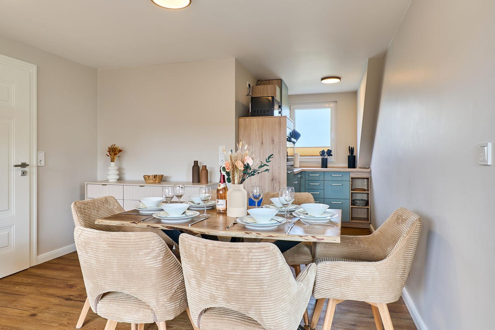 Essbereich mit Holztisch, sechs Stühlen und Küchenbereich im Hintergrund.