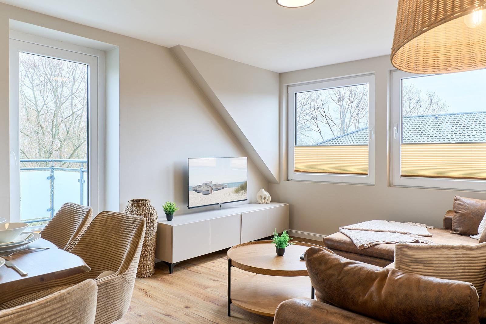Wohn- und Essbereich mit TV, Sofa und Tisch. Fenster mit Blick auf Balkon und Dach.