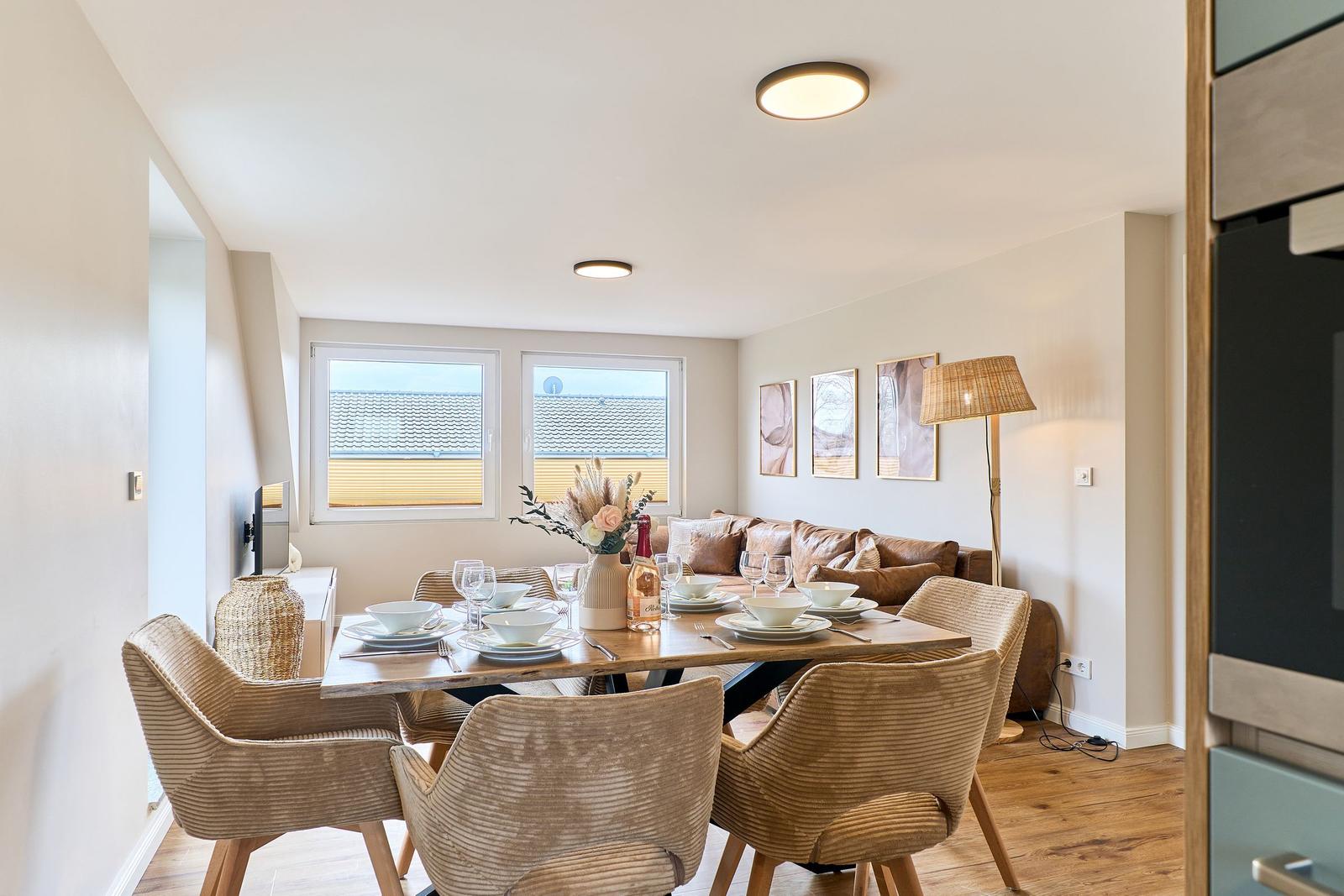Essbereich mit Tisch, Stühlen und Sofa. Fenster zeigen Dach und Wand.