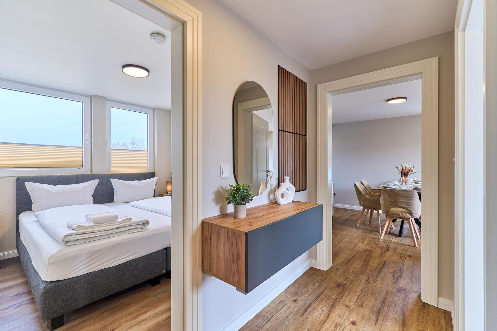 Schlafzimmer mit Doppelbett und Fenstern. Flur mit Wandkonsole und Spiegel. Esszimmer mit Tisch und Stühlen.