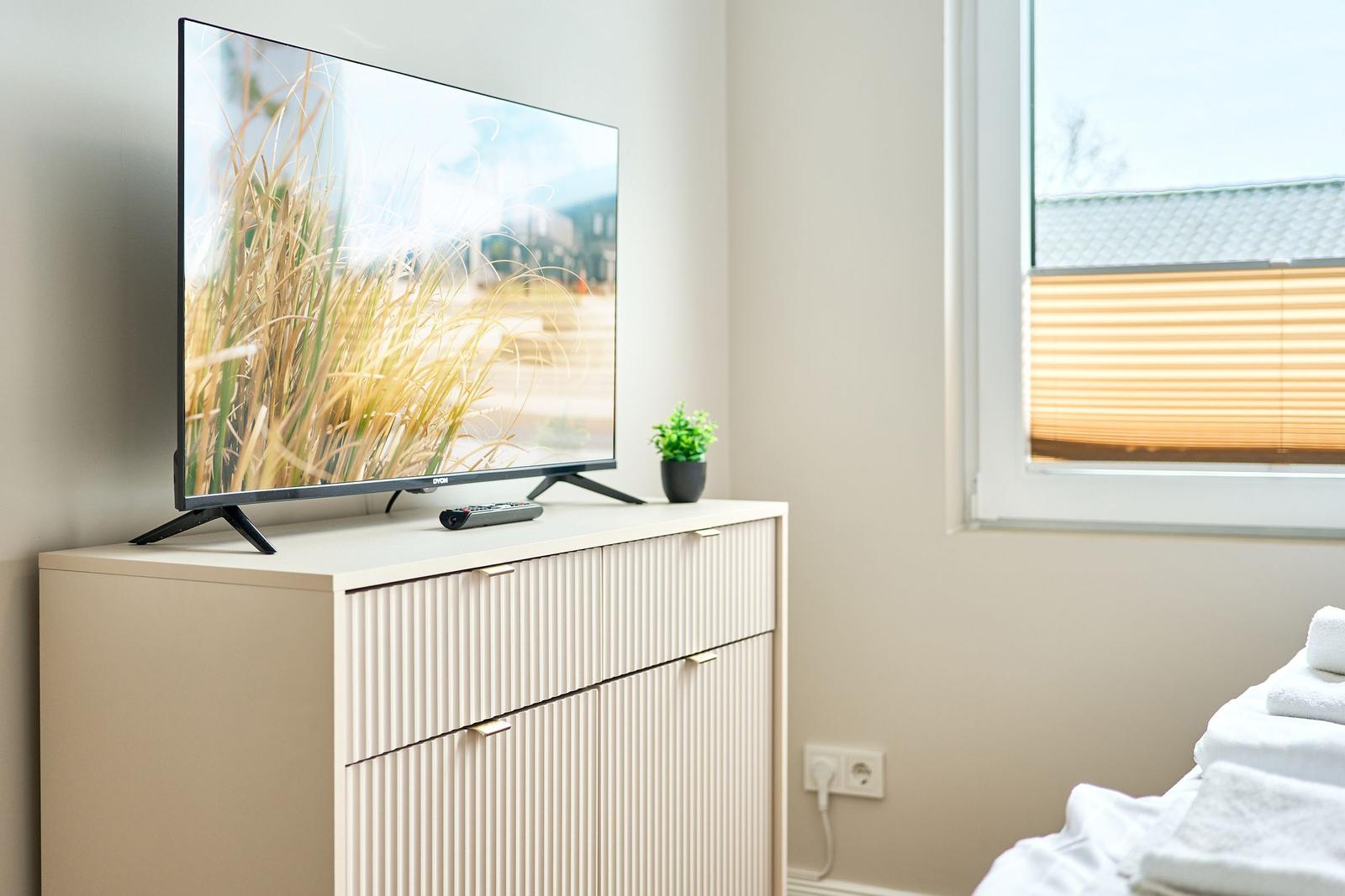 TV auf Schrank neben Fenster mit Jalousie und gestapelten Handtüchern