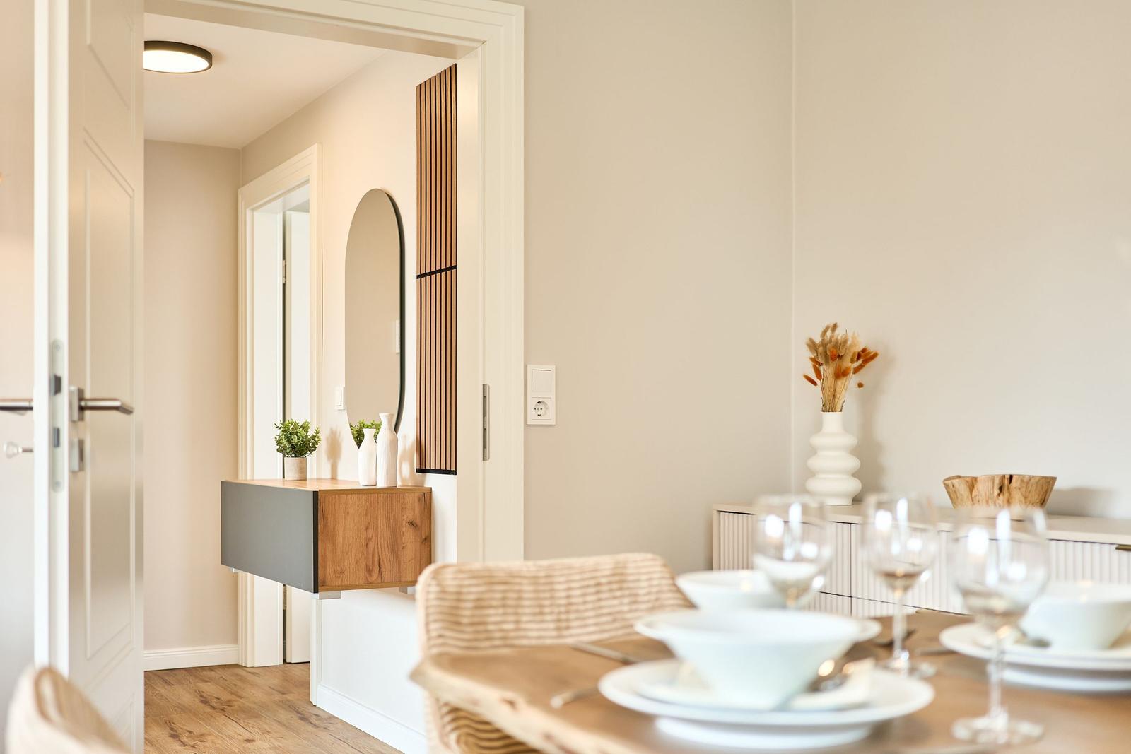 Essbereich mit Tisch und Stühlen. Im Hintergrund Flur mit Spiegel und Holzregal.