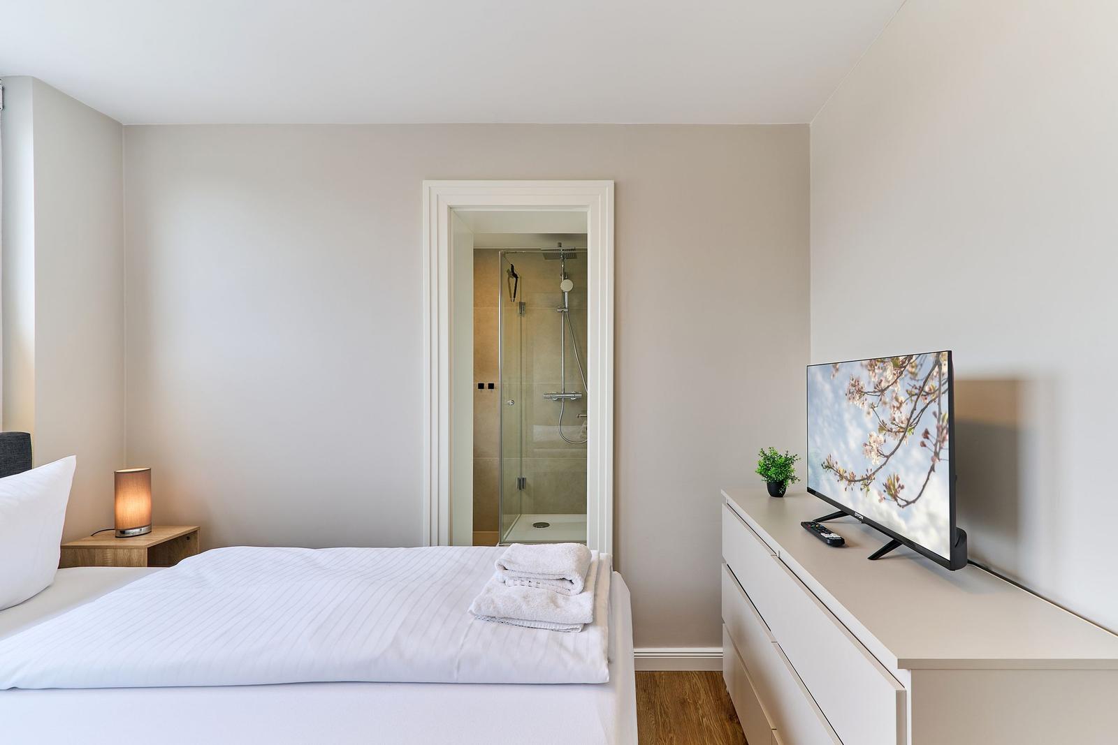 Schlafzimmer mit Bett, Fernseher und Blick in die Dusche.