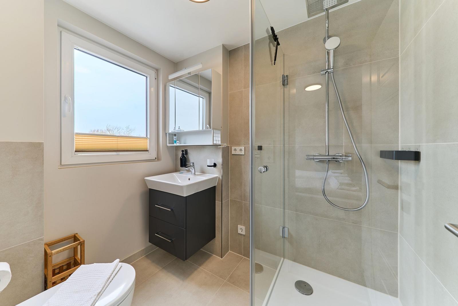 Badezimmer mit Dusche, Waschbecken und Fenster.