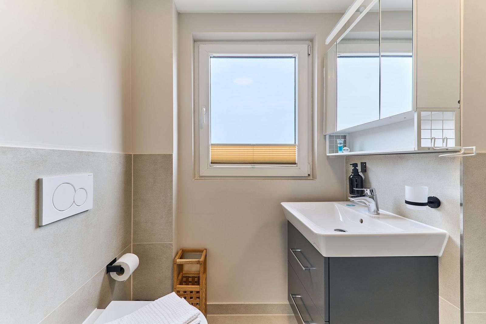 Badezimmer mit Waschbecken, Spiegelschrank und Fenster mit Jalousie.
