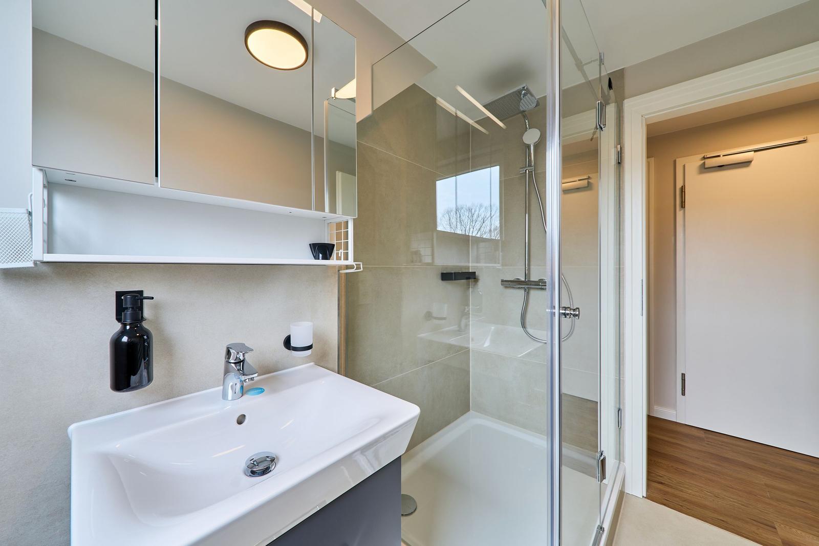 Badezimmer mit Dusche, Waschbecken und Spiegelschrank.